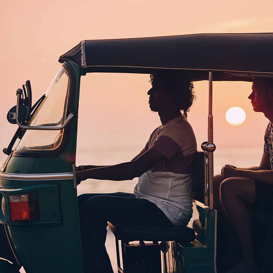 At dusk, one person is driving in the car and there is a person in the back seat.