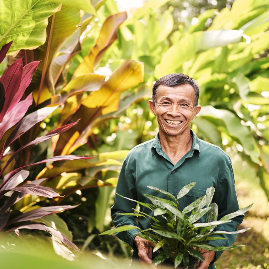 A local gardener smiling and holding a plant at Som Garden inside Chiva-Som in Hua Hin, Thailand 