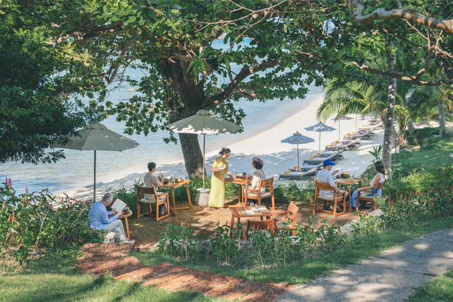 A group of people enjoy the day under the tree with umbrellas and picnic tables in the garden at Kamalaya in Koh Samui, Thailand