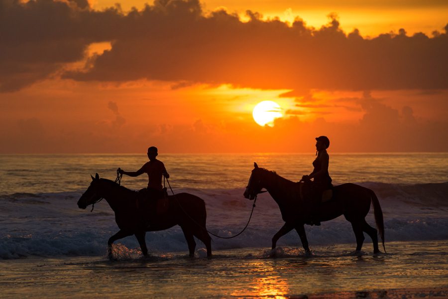 A couple horseback riding on the beach by the sea during sunset at Nihi Sumba, in Sumba, Indonesia