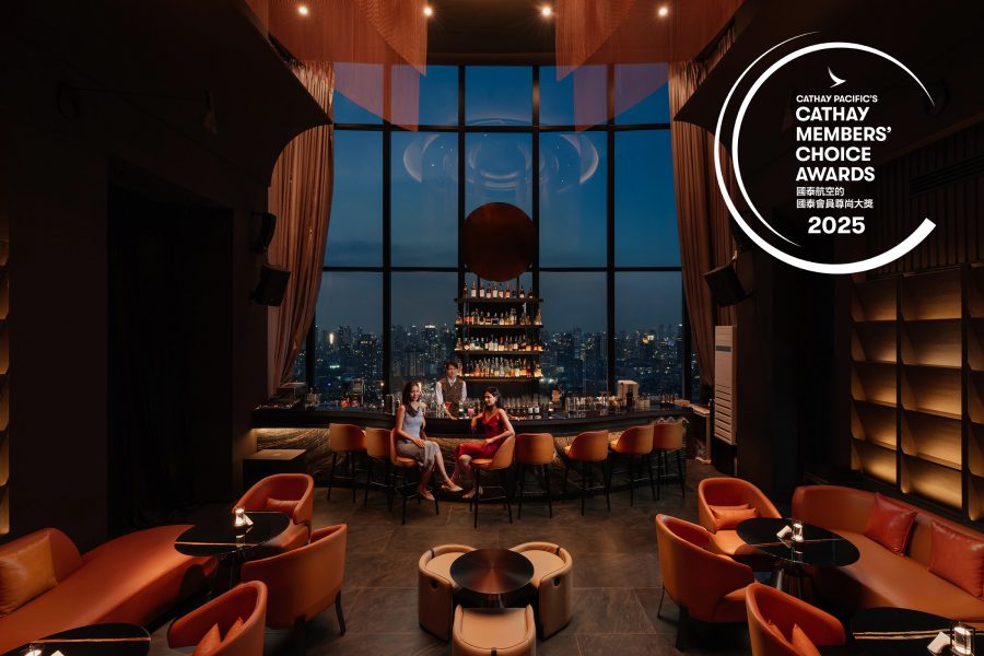 Two women sitting and a bartender behind the bar at Cielo Sky bar & restaurant with a view of Bangkok skyline in the background seen through the floor-to-ceiling windows