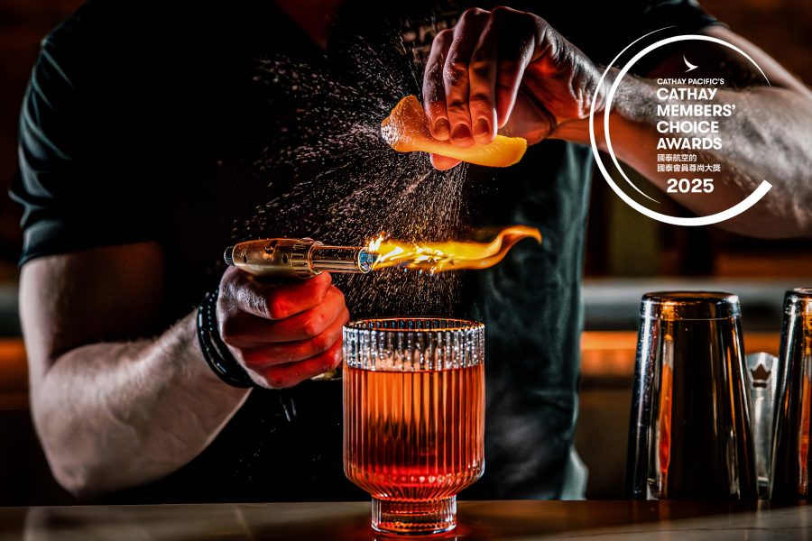 A closeup of a bartender squeezing orange zest over a flaming torch to make an old fashioned in a glass with ice
