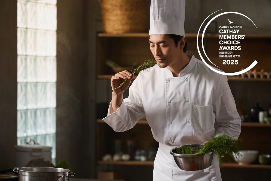 A chef in a kitchen holding a steel bowl while holding up herbs and smelling
