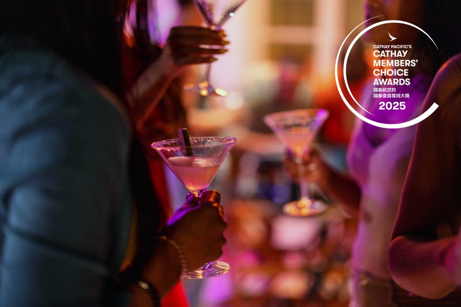 A group of women holding martini glasses gather around in a circle under neon purple lighting.