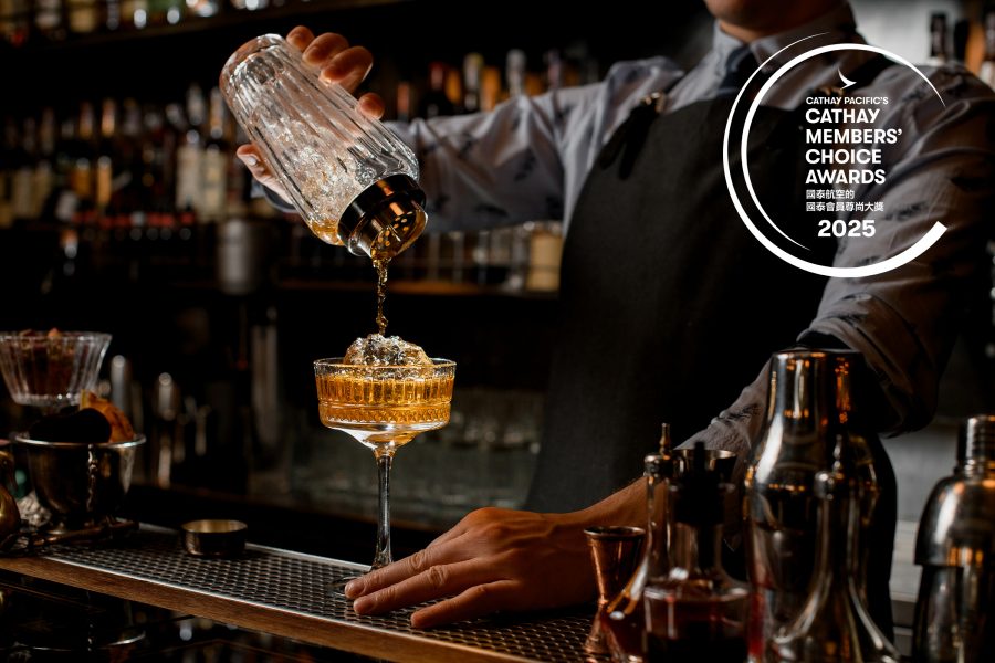 A bartender pouring an amber drink into a cocktail glass from a shaker.