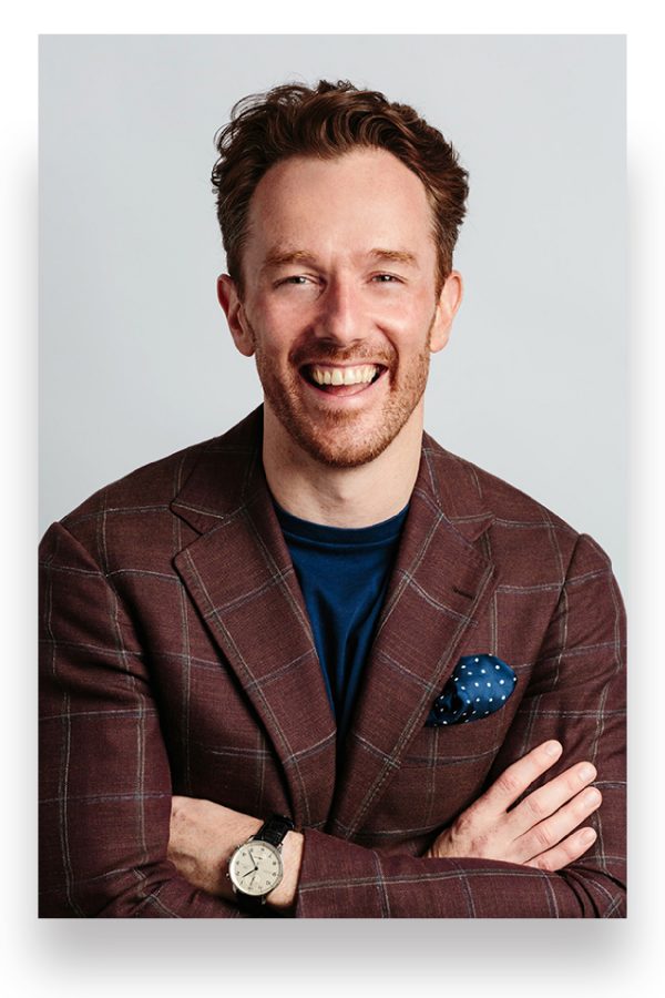 Fork Lore founder Simon Wilson smiles for the camera wearing a brown plaid suit.