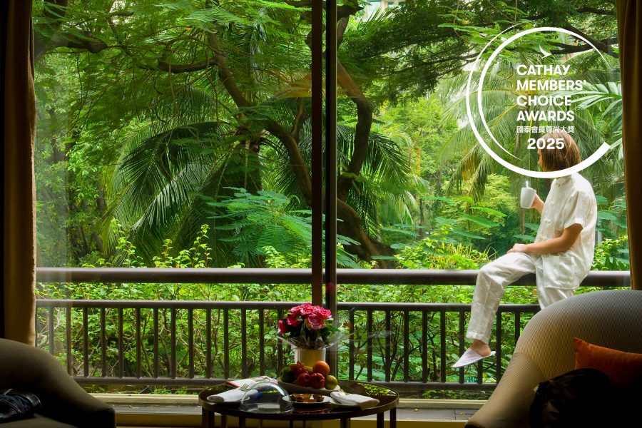 Woman sitting on a terrace balcony holding a cup, against a jungle backdrop outside her hotel room.