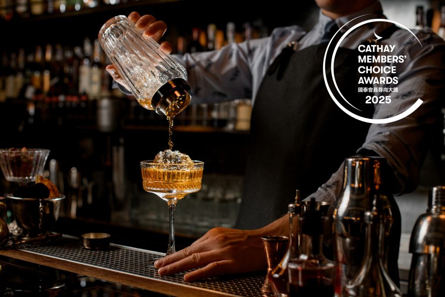 A bartender pouring an amber drink into a cocktail glass from a shaker.