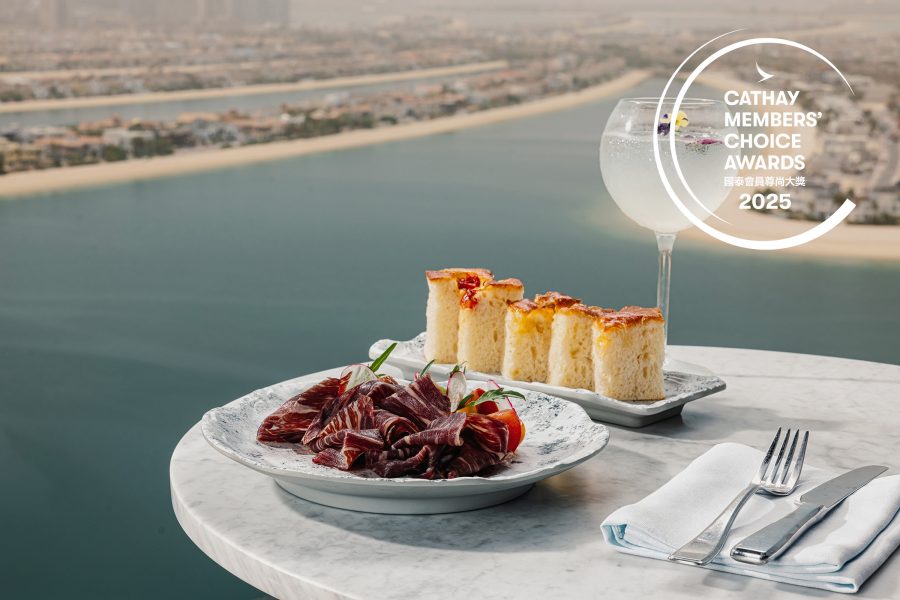 A plate of cold cuts, foccacia slices and a cocktail goblet on a marble table overlooking the coastline.