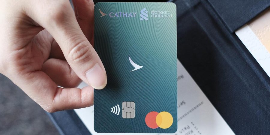 A hand holding a contactless  Standard Chartered Cathay co brand credit card with Cathay and Standard Chartered logos, and Mastercard logo.