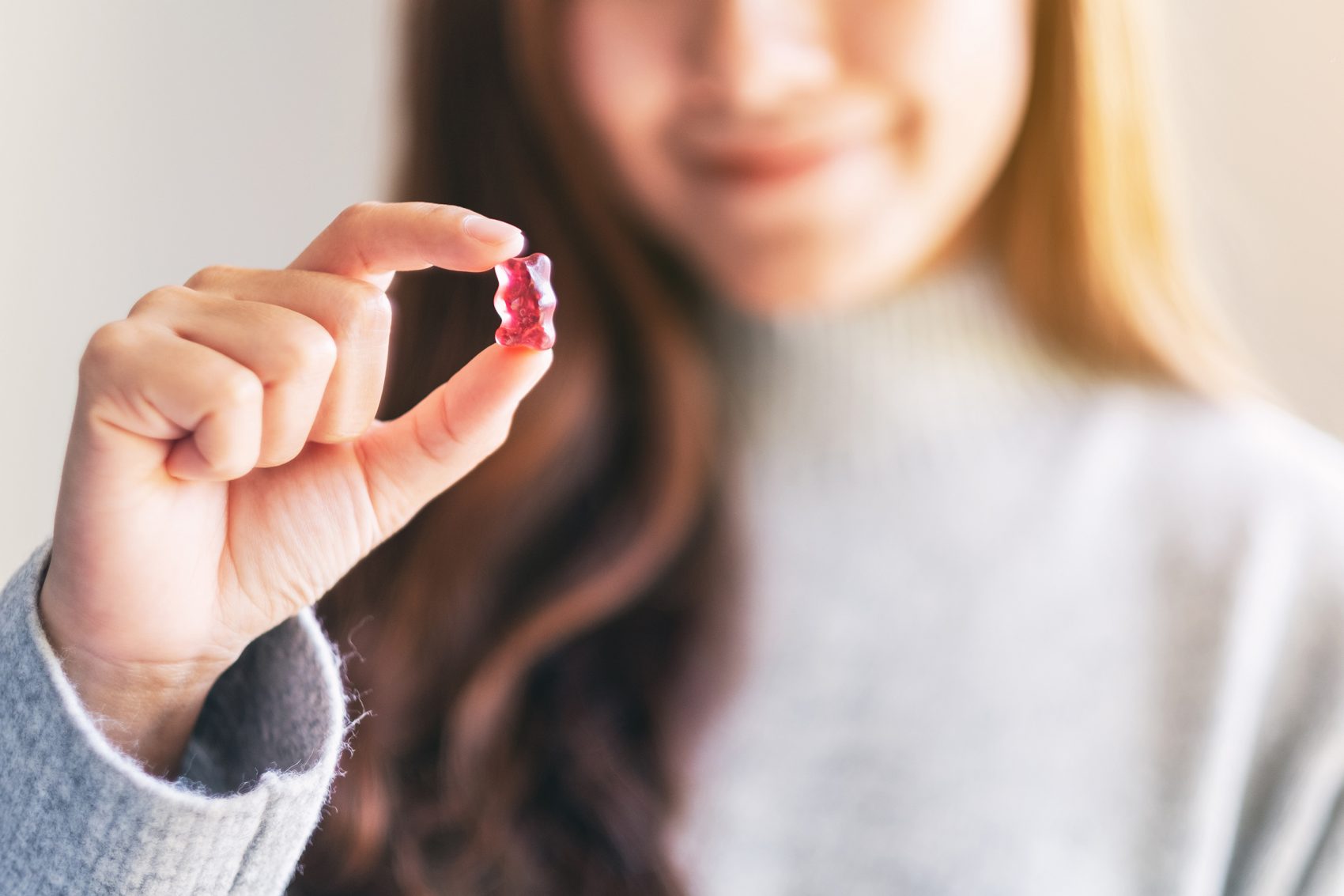 A woman holding up a red gummy bear between the fingers