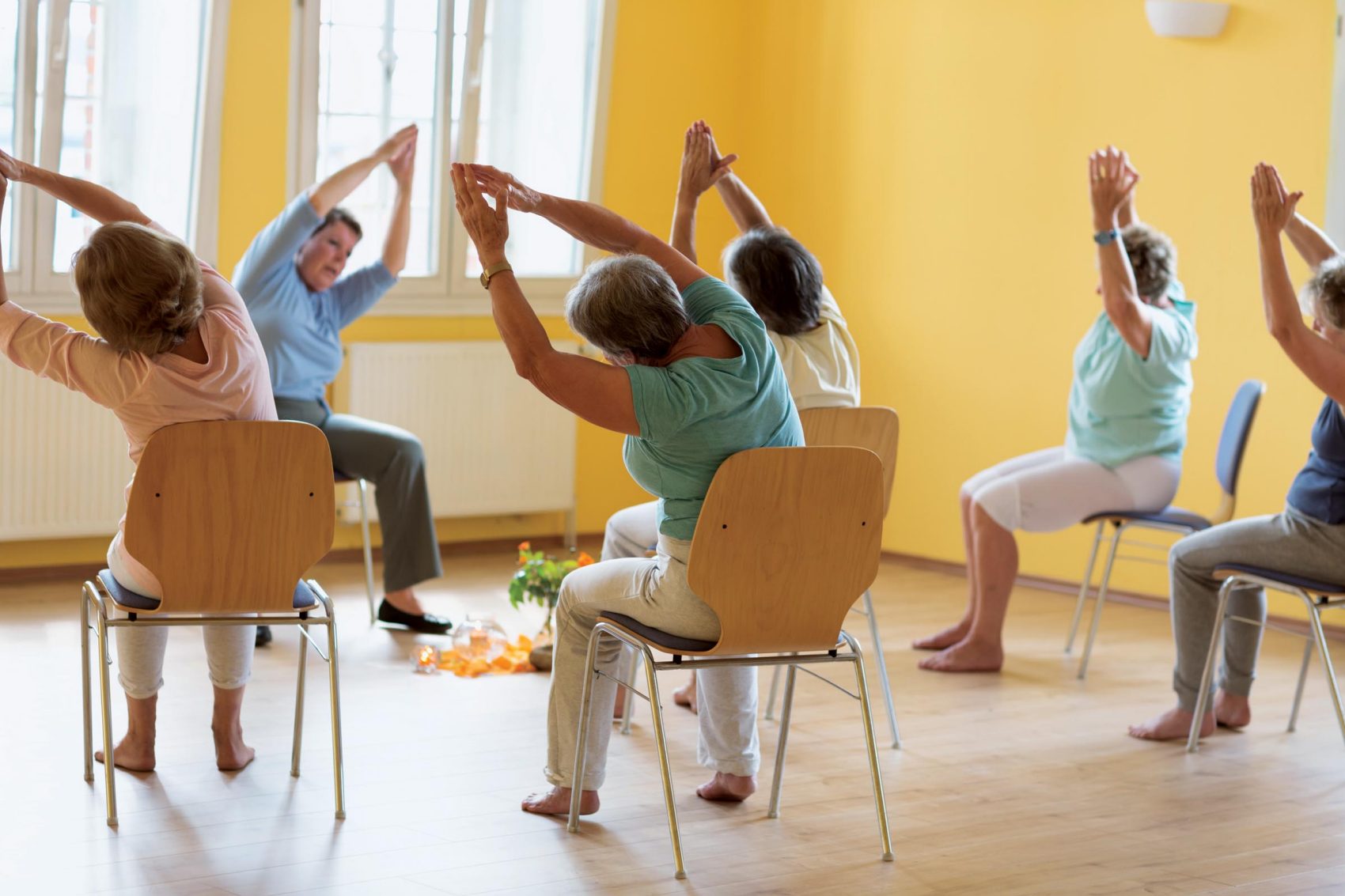 Class of elderly people practising chair yoga