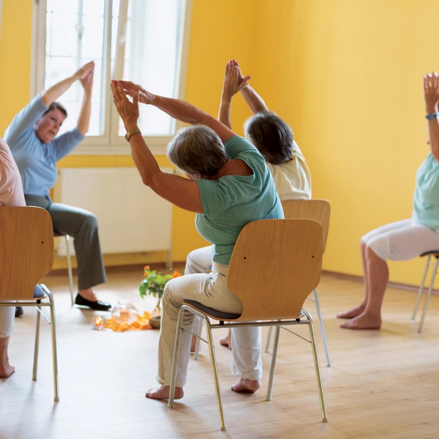 Class of elderly people practising chair yoga