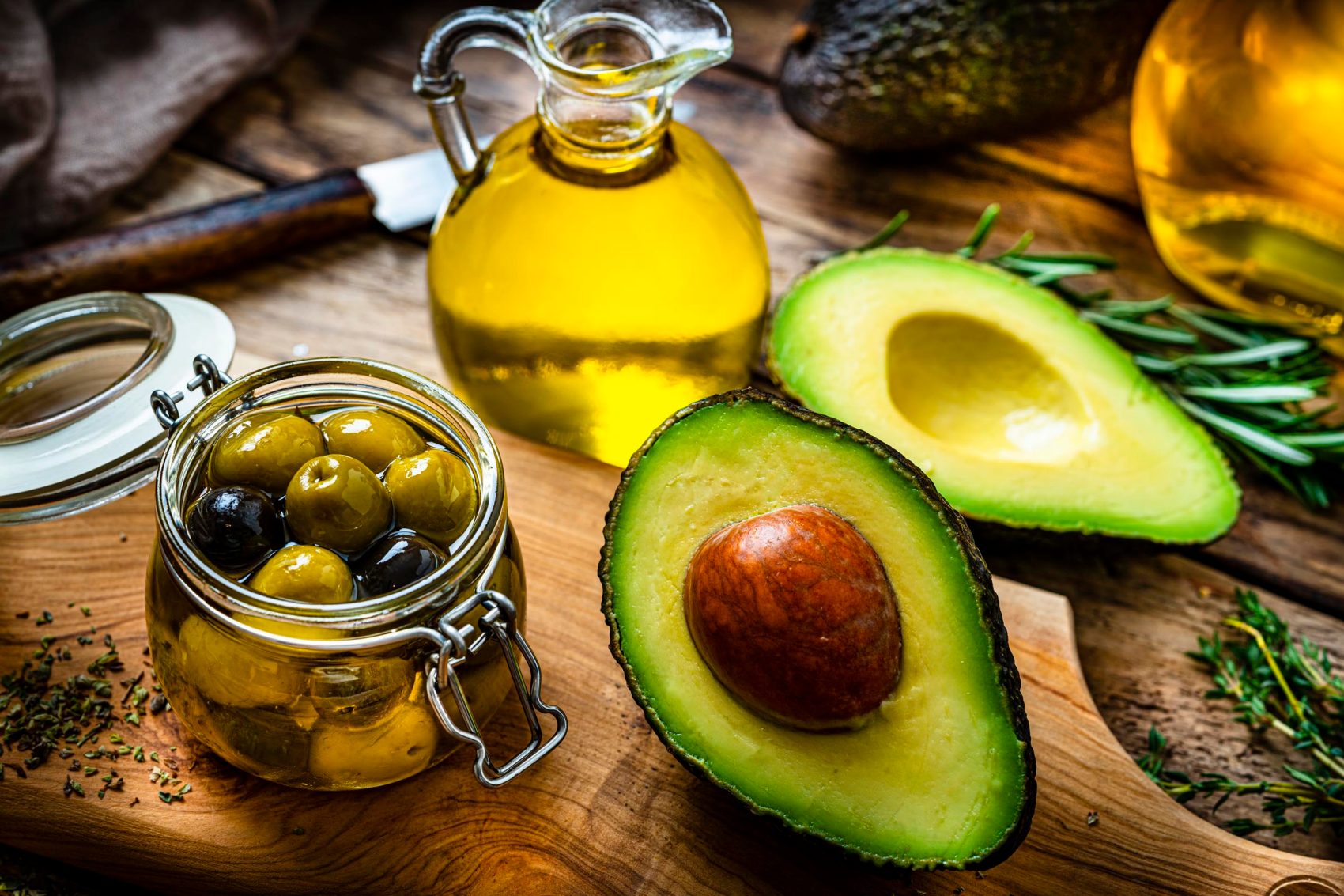 Avocado, a jar of olives and small jug of oil olive on a table