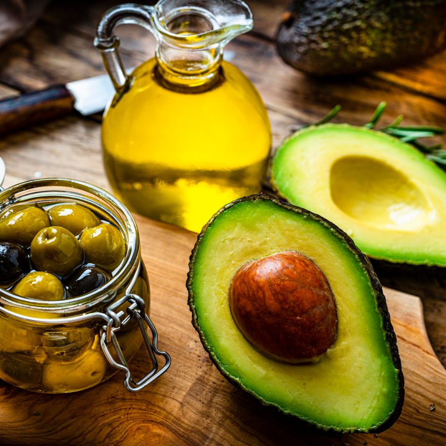 Avocado, a jar of olives and small jug of oil olive on a table