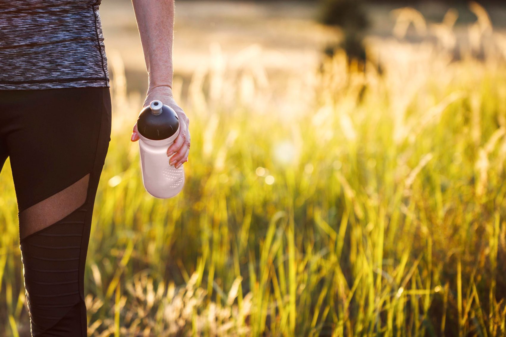 Person holding a reusable water bottle while walking through long grass