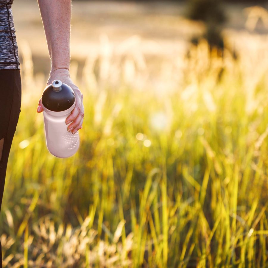 Person holding a reusable water bottle while walking through long grass