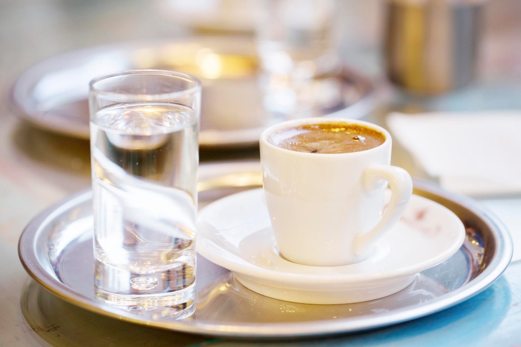 Glass of water and cup of coffee served on a round silver tray