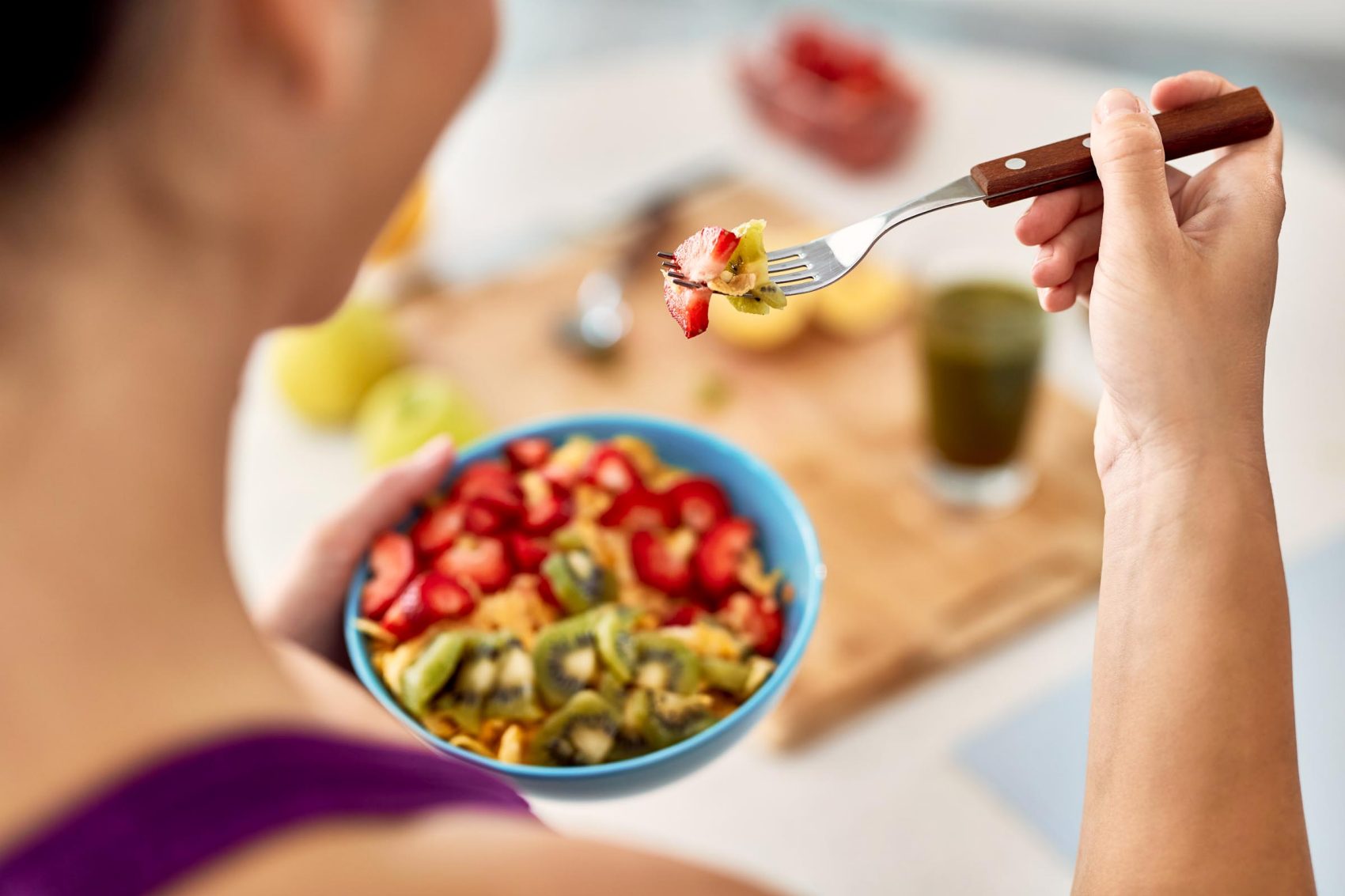 A person eating a bowl of mixed fruits