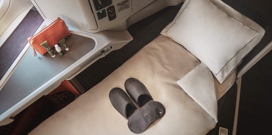 Image of a flatbed on an aircraft. The frame showcases a pair of slippers and other items from the Cathay's amenity kit.