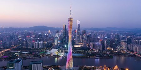 Panoramic view of Guangzhou's city skyline at night. At the centre is the Canton Tower lit up in rainbow colours.