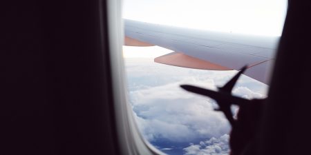 Silhouette of a hand holding a small model of a plane against the window of a Cathay Pacific aircraft. 