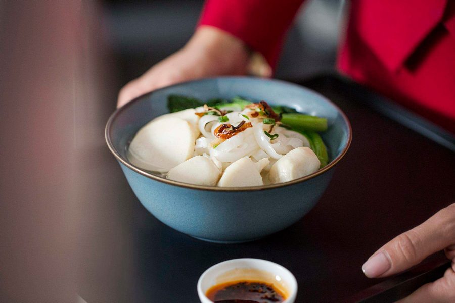 A flight attendant serving a bowl of fish ball noodles on a black tray.