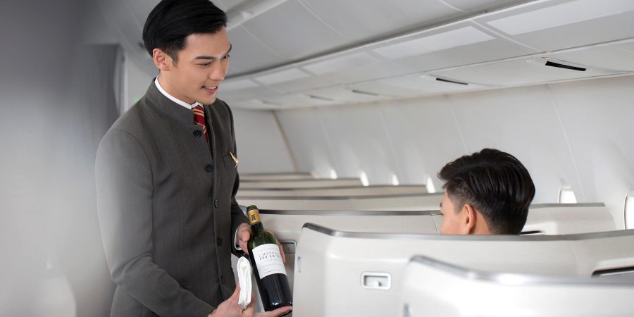 一名国泰航空机组人员正将一瓶葡萄酒放在一位坐在商务舱座位的乘客面前。