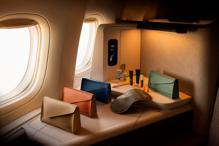Four available colours of the inflight Bamford amenity kit, sleep accessories and skincare and toiletries arranged on a ledge by the window inside the Cathay Pacific Aria Suite. 