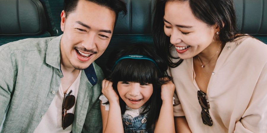 A young girl with headphones on sat between a man and woman on a Cathay Pacific flight.