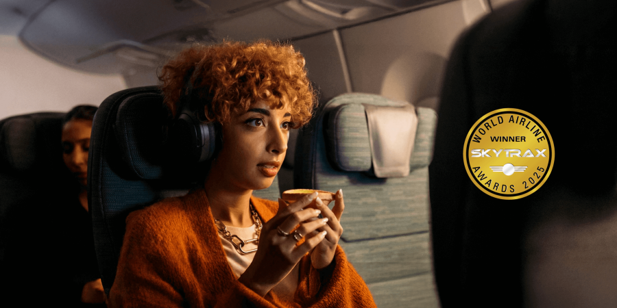 一名戴著耳機的女乘客坐在國泰航空經濟艙內，手持一杯飲料，觀看前方座椅背面的屏幕。