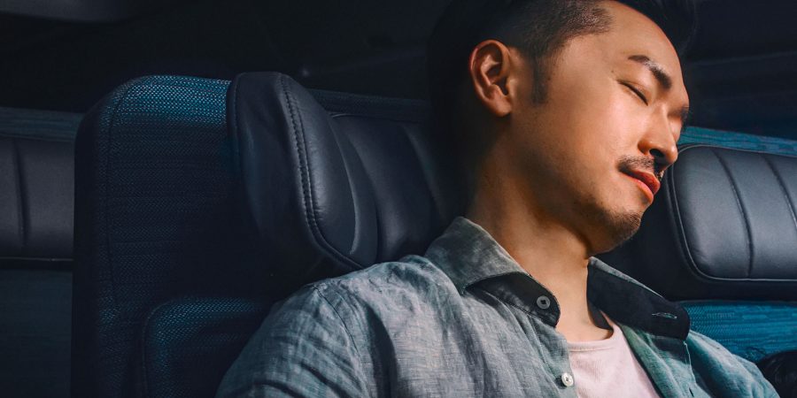 A male passenger asleep with his head against the headrest in one of Cathay Pacific's Economy seats.