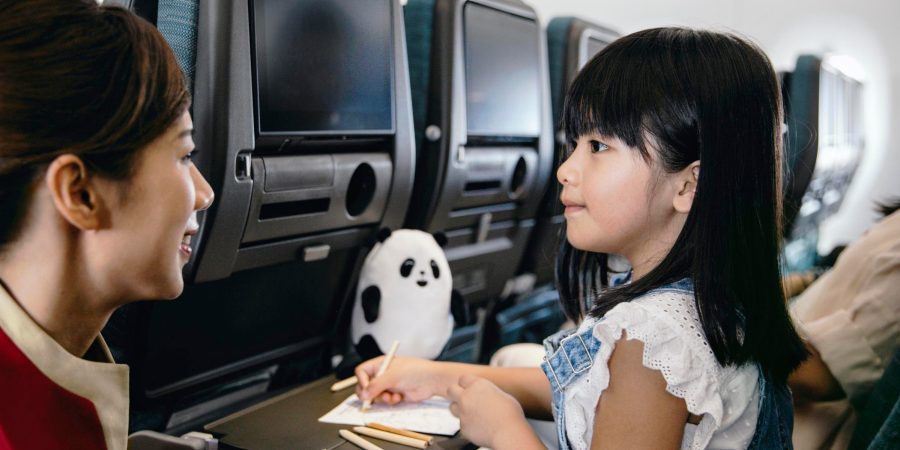 A Cathay Pacific cabin crew attending to a young girl on board. The girl is colouring in a colouring book.