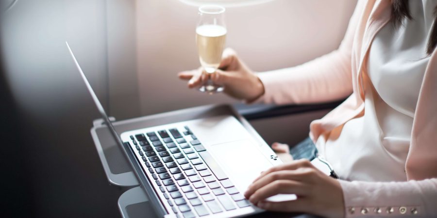 A female passenger, seated in Cathay Pacific's Premium Economy cabin,  holds a glass of champagne while browsing her computer.