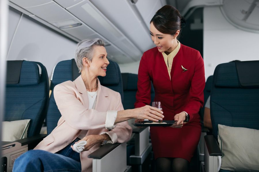 A Cathay Pacific flight attendant serving a drink to a passenger on board. The two are smiling at each other.