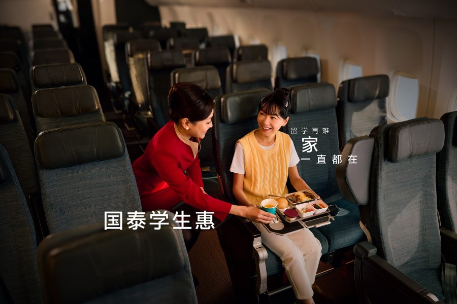 在一架国泰航空飞机客舱内，空乘人员正为一名中国留学生送上美味中式机飞机餐，并微笑着与乘客交谈。国泰航空学生机票助力海外求学之旅，让您在万米高空也能感受家的温暖。