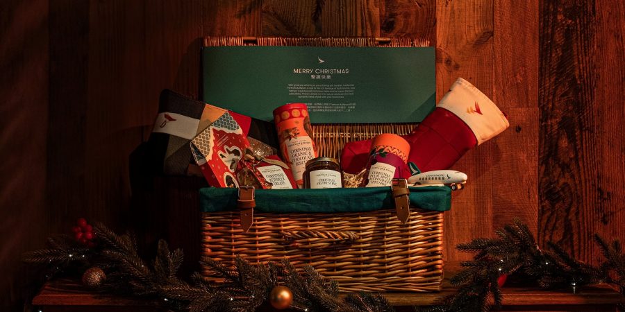 Close-up of a Cathay Christmas hamper filled with biscuits, tea, jam and other treats. The hamper is sitting on a wooden cabinet decorated with a Christmas garland.