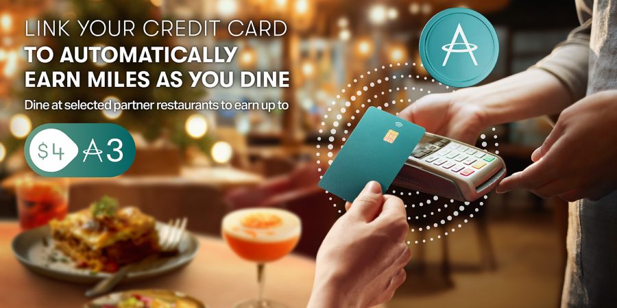 Close-up of a hand using a credit card on a contactless payment terminal. In the background, a cocktail and lasagne dish are sat on a table in a restaurant.