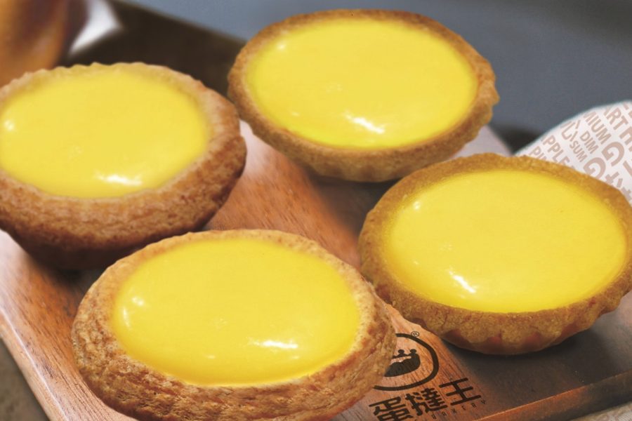 Close-up of four egg tarts on a wooden cutting board.