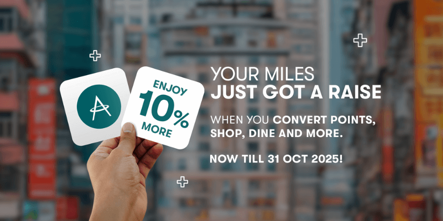 A hand holding two cards in front of a blurred cityscape. One card features a logo with an 'A' and an arrow, while the other reads 'ENJOY 10% MORE.' Promotional text on the image says: 'YOUR MILES JUST GOT A RAISE WHEN YOU CONVERT POINTS, SHOP, DINE AND MORE. NOW TILL 31 OCT 2025!