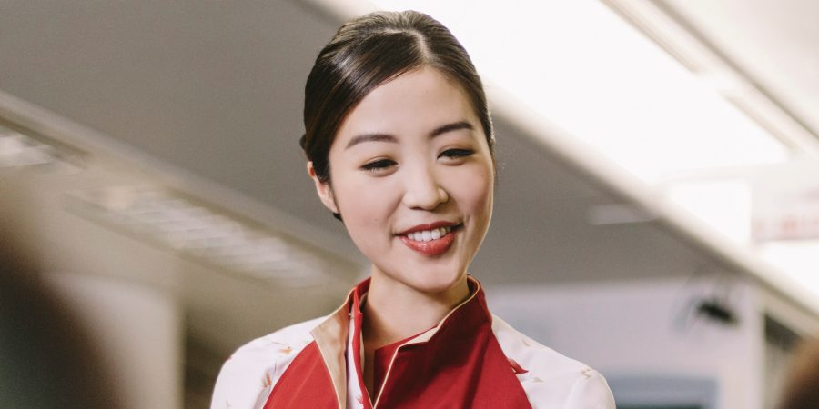 A Cathay Pacific cabin crew smiles while attending to a passengers in Economy cabin.