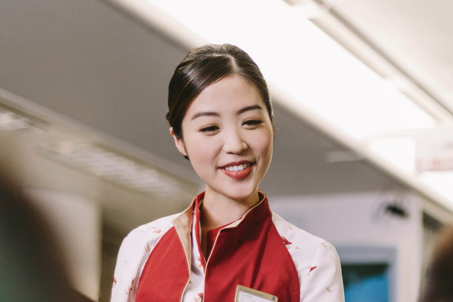 一名面帶微笑的國泰航空機艙服務員正為經濟客艙乘客服務。